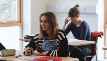 0S7A7994 Two students sitting in a classroom; female student in black and white striped shirt is looking up and forwards. CertHE Gaelic and Communication class, 2022.